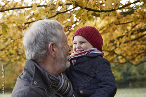 Grandfather Cuddling Granddaughter On Autumn Walk