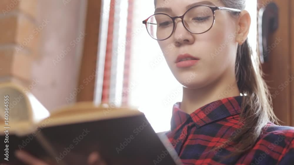 Attractive woman in eyeglasses reading book standing at window Attractive woman in eyeglasses reading book standing at window