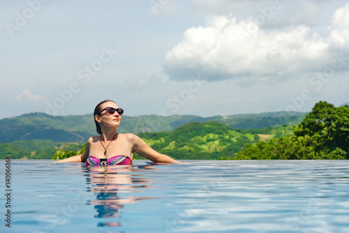 young pretty woman enjoying resting on the edge of outdoor swimming pool. © soft_light