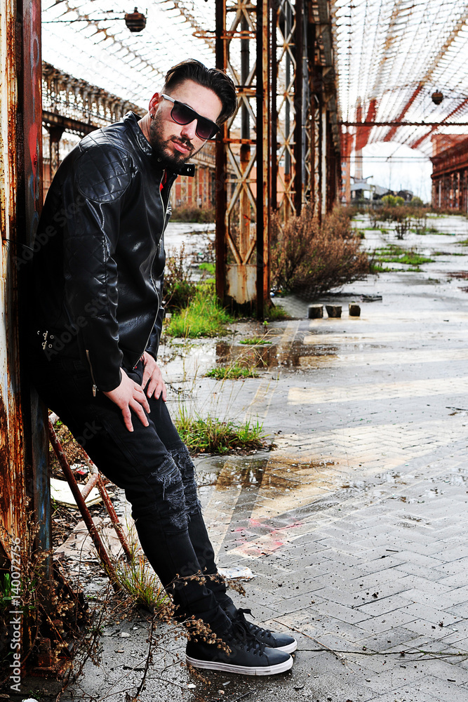 young trendy man with leather jacket, red shirt and black pants with low  waist. background metropolitan Stock Photo | Adobe Stock