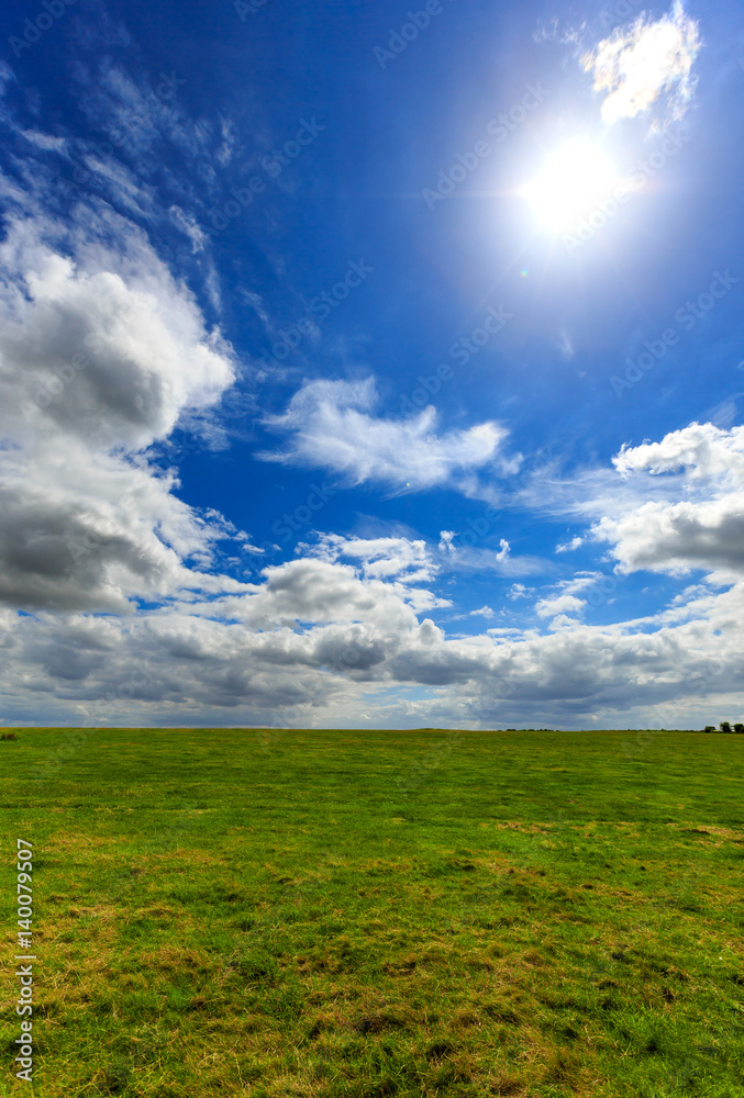 Realistic blue cloudy sky with bright sun over green meadow field