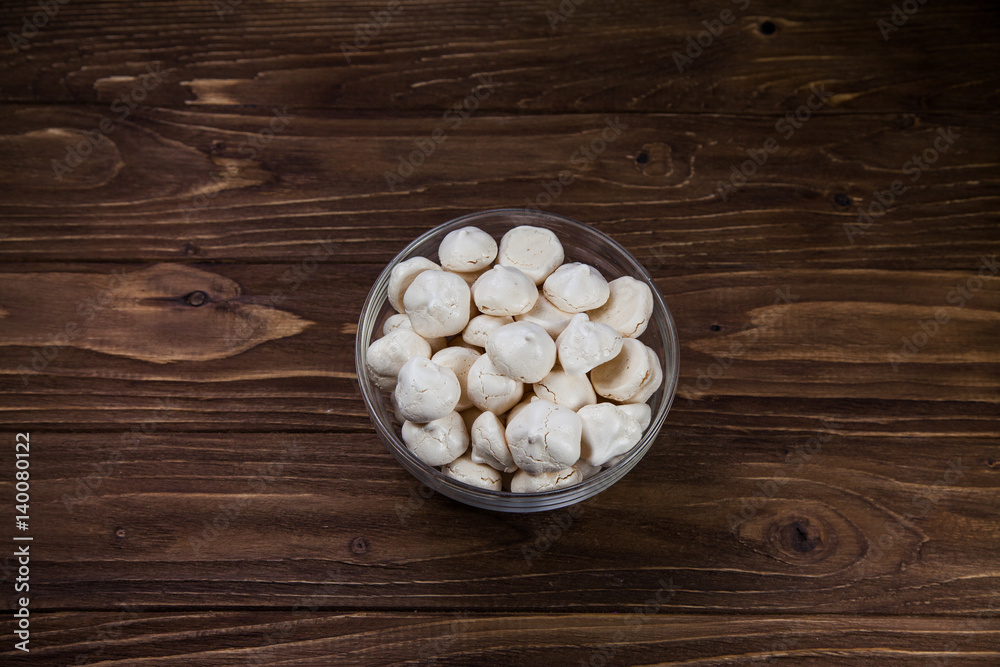 White mini meringue in transparent vase on brown wooden background White mini meringue in transparent vase on brown wooden background