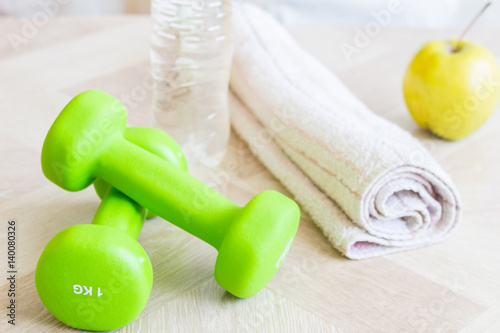 Green dumbbells, water bottle, apple and a towel. Set for sports. The concept of sport, a healthy lifestyle.