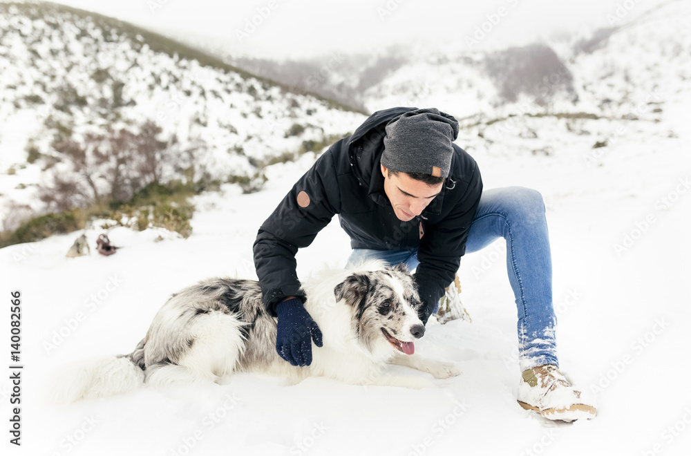 Young man stroking his dog in the snow Young man stroking his dog in the snow