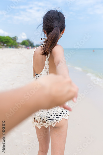 Woman holding man's hand and leads to the sea