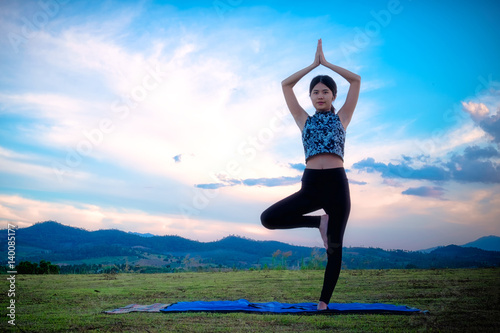 Woman practicing yoga pose outdoors over sunset sky background.