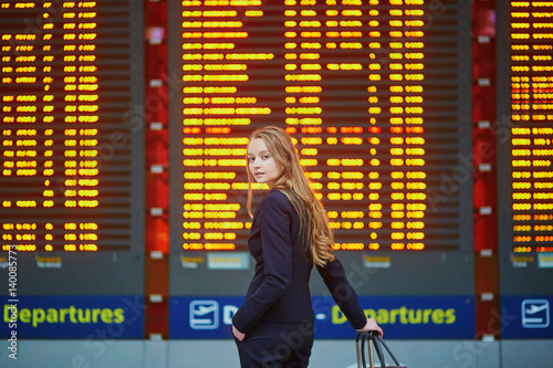 Woman with hand luggage in international airport terminal, looking at information board