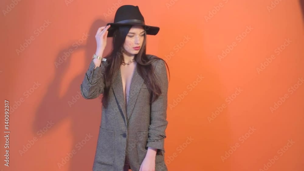 Young female in jacket posing and touches the hat, casts a shadow on the wall Young female in jacket posing and touches the hat, casts a shadow on the wall