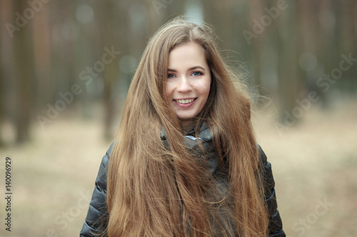 Close up portrait of smiling beautiful young woman with gorgeous extra long hair posing in spring park windy weather outdoors