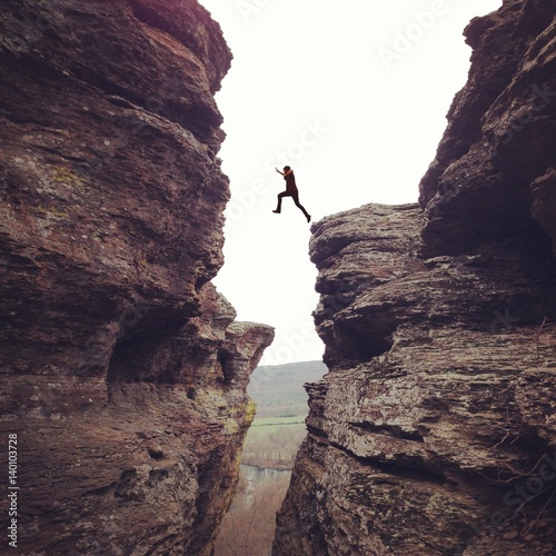 Person in mid air, leaping in between cliffs 
