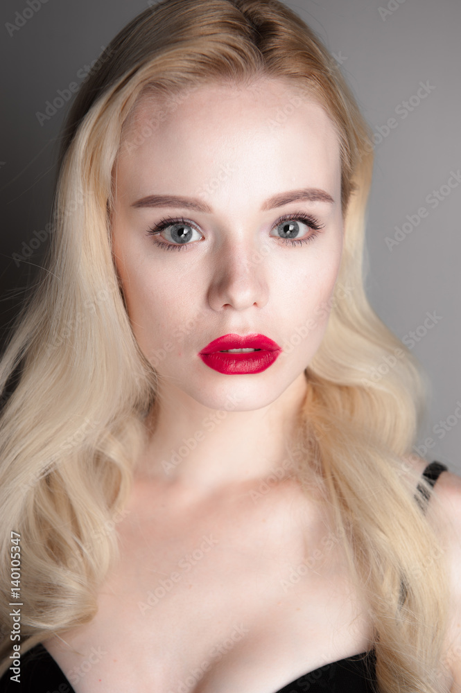 Beauty model girl with perfect make-up red lips and blue eyes looking at camera. Portrait of attractive young woman with blond hair. Beautiful female face with clear fresh skin. Fashion close up shot.