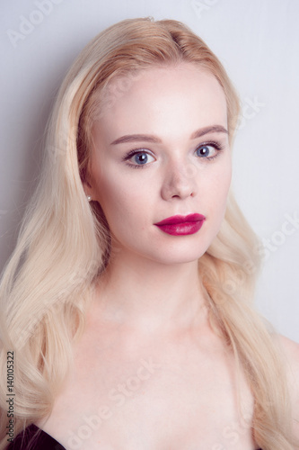 Beauty model girl with perfect make-up red lips and blue eyes looking at camera. Portrait of attractive young woman with blond hair. Beautiful female face with clear fresh skin. Fashion close up shot.