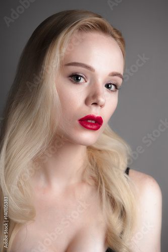 Beauty model girl with perfect make-up red lips and blue eyes looking at camera. Portrait of attractive young woman with blond hair. Beautiful female face with clear fresh skin. Fashion close up shot.