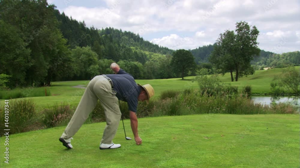 Golfer teeing up ball, hitting it down fairway, and walking out of frame at left Golfer teeing up ball, hitting it down fairway, and walking out of frame at left
