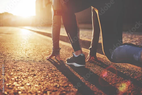 Obraz Atlety kobieta w bieg początku pozie na miasto ulicie. Sportowe ciasne ubrania. Jasny zachód słońca, rozmyte tło. Poziomy