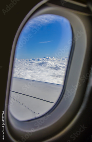 Airplane porthole view. View of airplane wing and cloudscape.