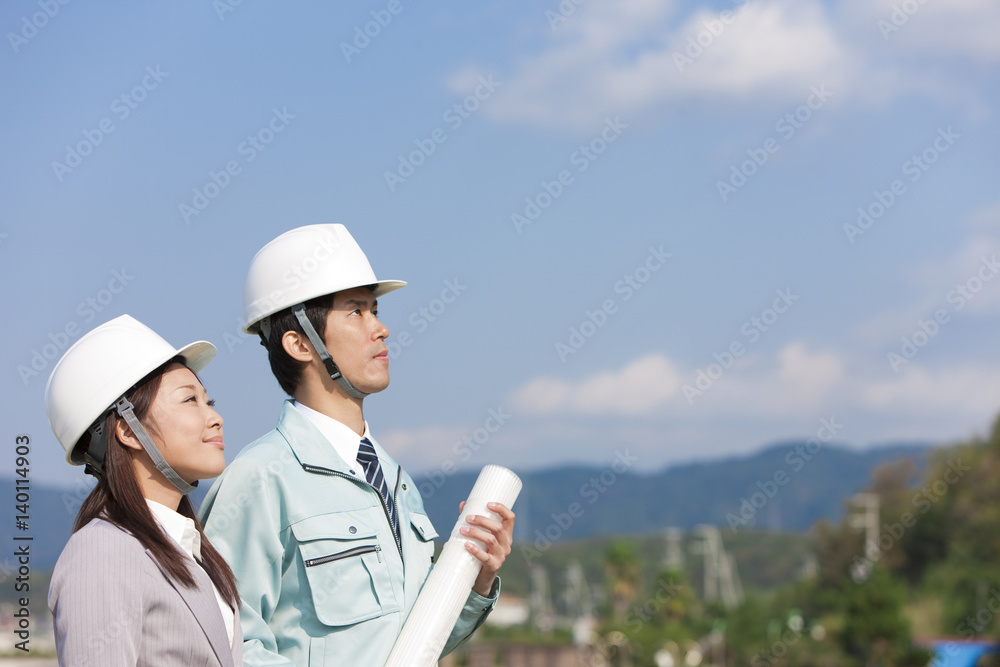 Engineers holding blueprint and looking up at construction site Engineers holding blueprint and looking up at construction site