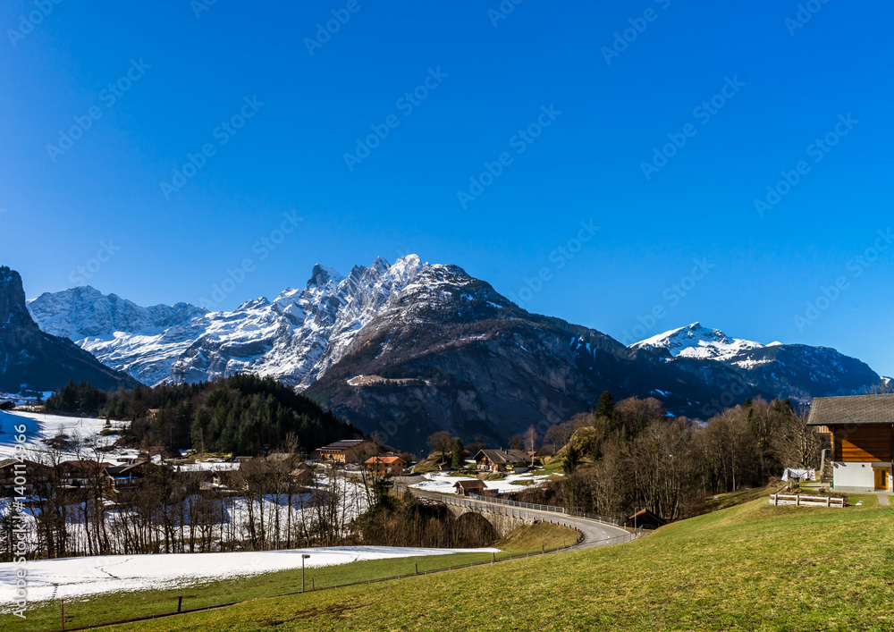Alpine natural landscape with green fields, high rocks and white clouds
