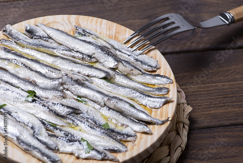 Tasty anchovies next to a fork on wooden table. Horizontal shoot.
