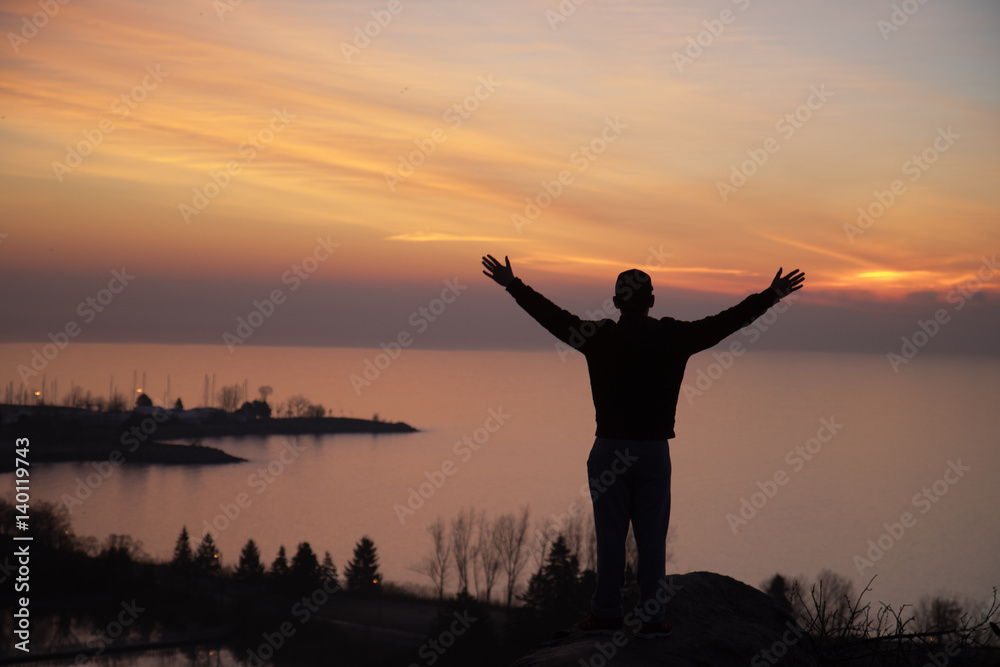 silhouette of man with open arms overlooking water silhouette of man with open arms overlooking water