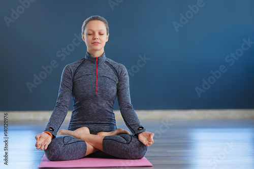 Beautiful young woman sitting in Lotos pose. woman practicing meditation in yoga hall after hard day. photo