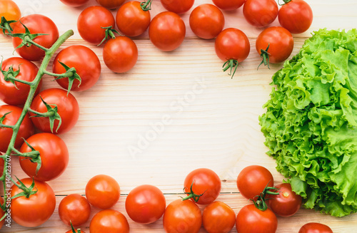 Ripe tomatoes and green lettuce on a wooden table form frame for text inside. Tomatoes on a branch