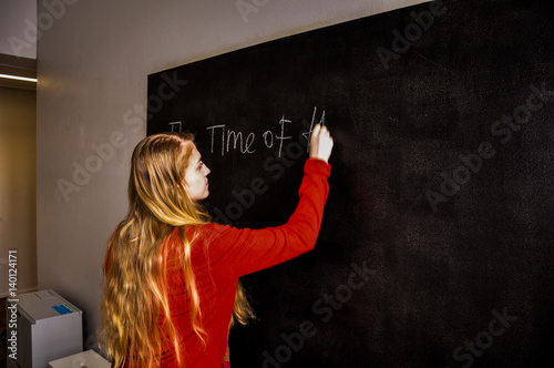 A young woman writes in chalk on a blackboard