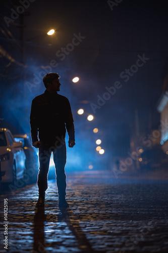 The man stand on the foggy street. Evening night time. Telephoto lens shot