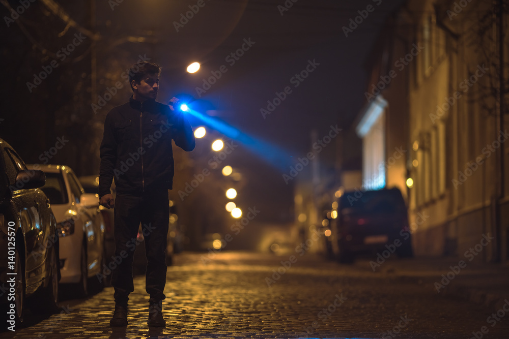 The man with a flashlight stand on the road. Evening night time