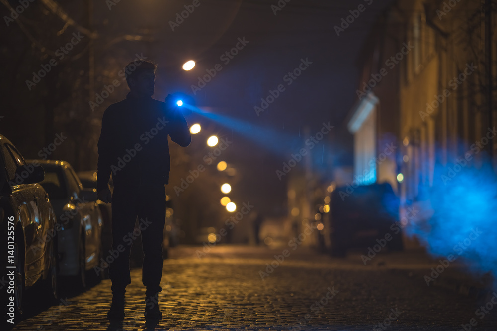 The man with a flashlight stand on the road. Evening night time