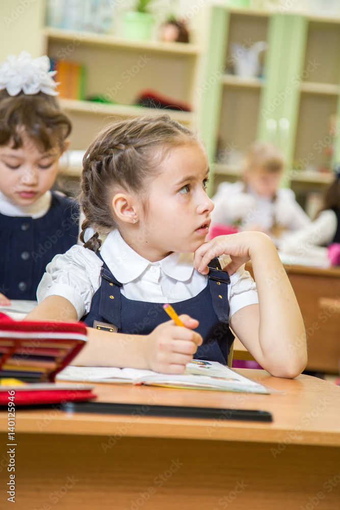 little beautiful schoolgirl in school uniform with brunette hair sitting on desk little beautiful schoolgirl in school uniform with brunette hair sitting on desk
