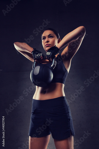 young woman flexing muscles with kettlebell in gym
