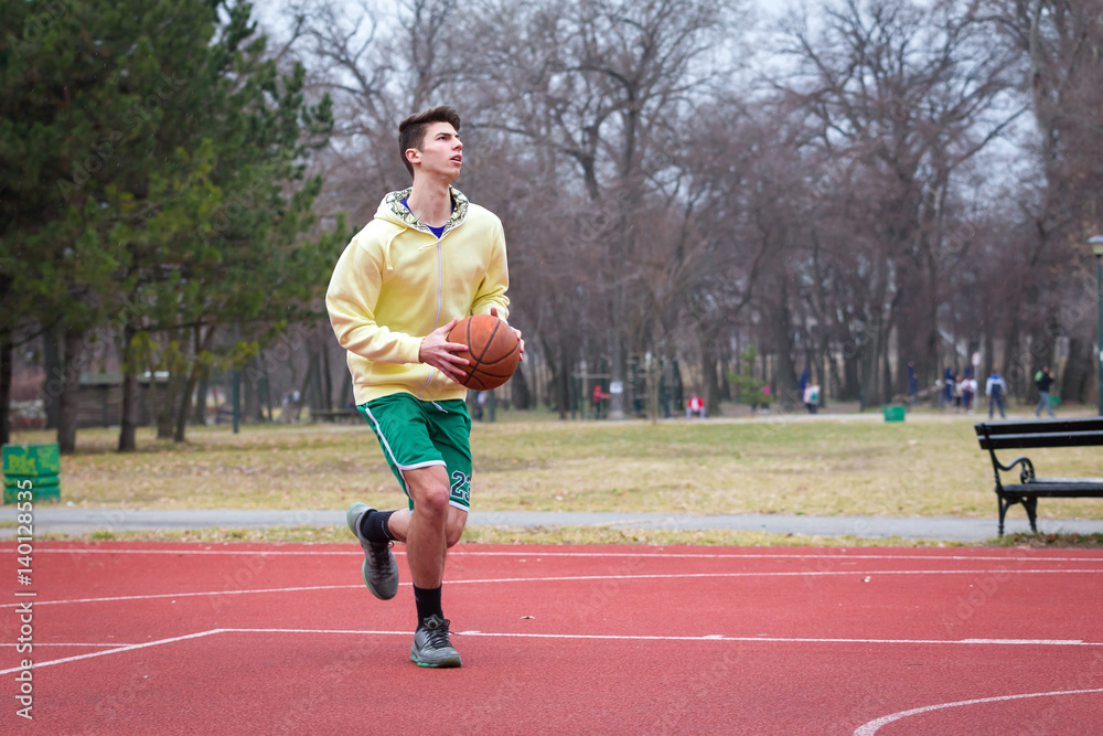 one ypung man plays basketball in a park