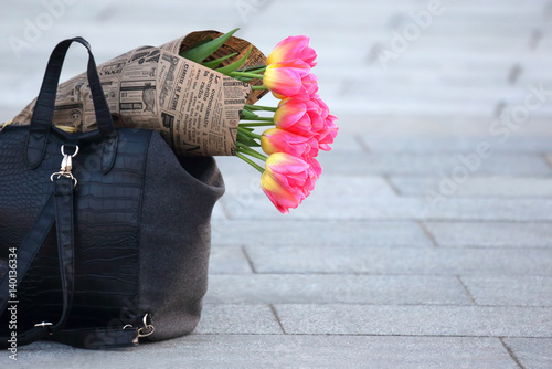 flowers tulips wrapped in newspaper lying in the women's bag.