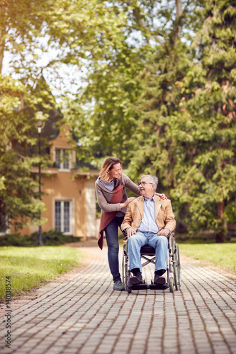 senior man in a wheelchair enjoying fresh air in a sunny day with his daughter.