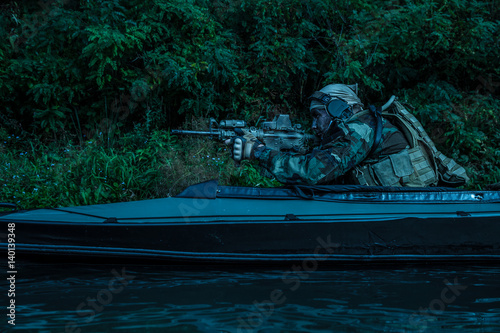 Special forces man with painted face in camouflage uniforms in army kayak. Seeking target, diversionary mission, twilight photo