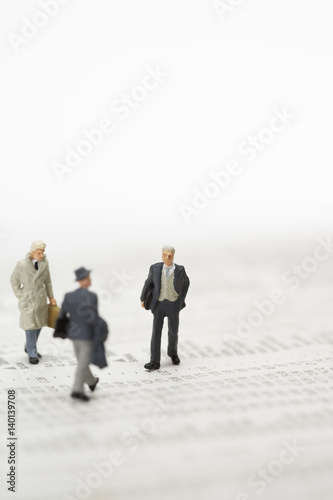 Three businessmen figurines walking over financial newspaper