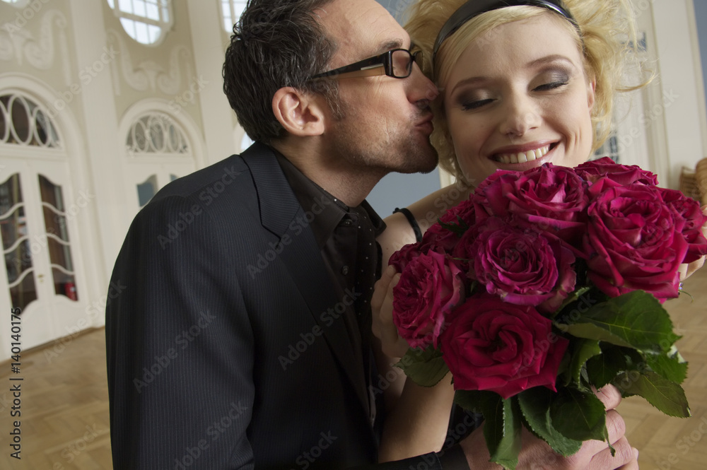 Man giving young woman a bunch of roses and kissing her Man giving young woman a bunch of roses and kissing her