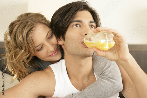 Young man drinking bottled juice  woman embracing him from behind