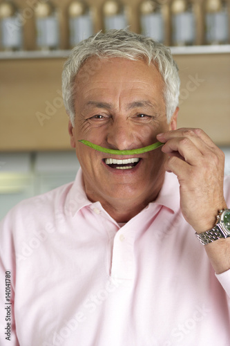 Gray-haired man holding a green bean under his nose, close-up