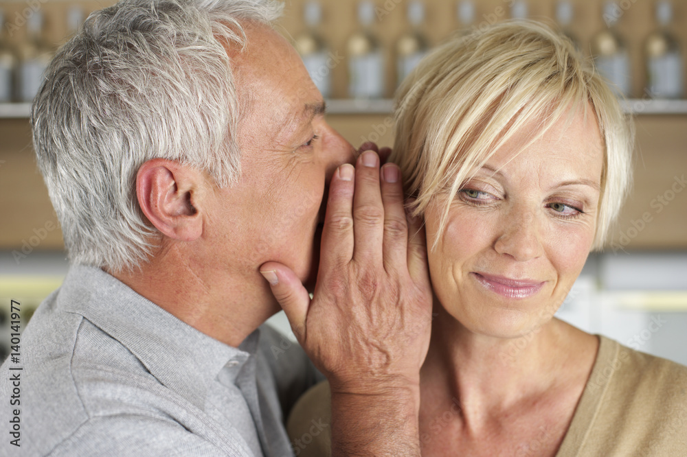 Gray-haired man whispering something into the ear of a woman, close-up Gray-haired man whispering something into the ear of a woman, close-up