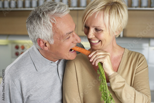 Blonde woman feeding a gray-haired man with a carrot, close-up