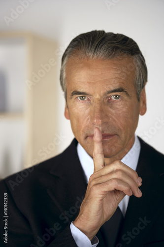 Obraz na plátně Senior businessman holding a finger in front of his mouth