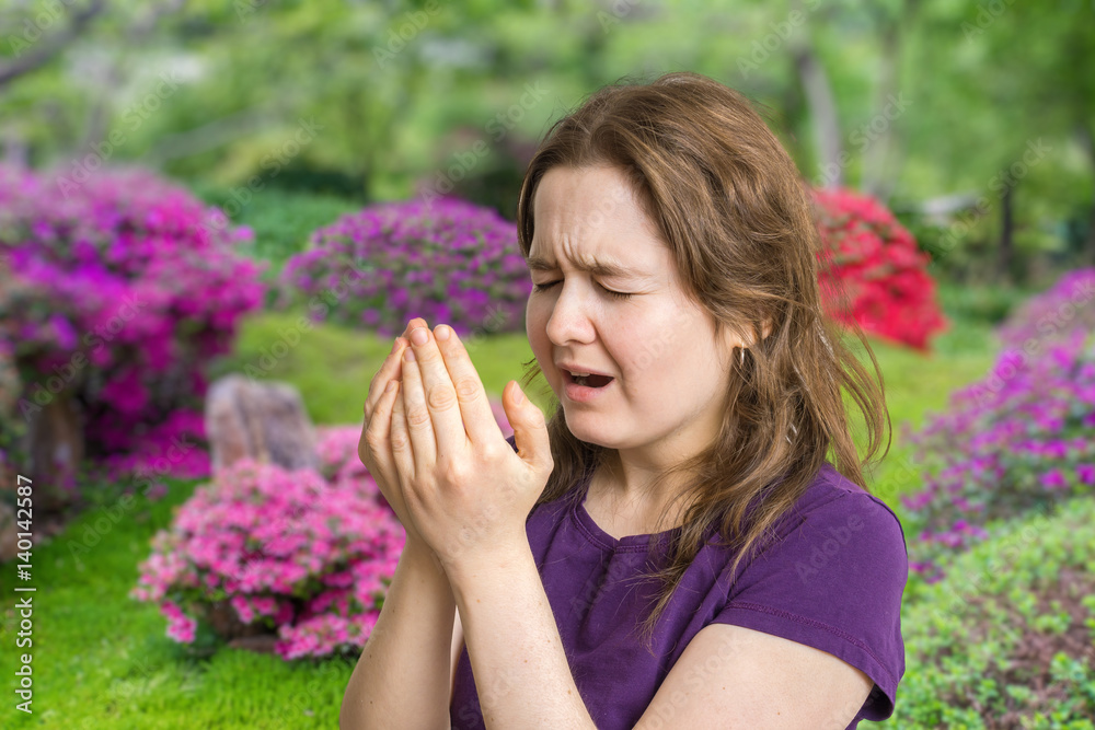 Fototapeta premium Pollen allergy concept. Young woman is going to sneeze. Flowers in background.