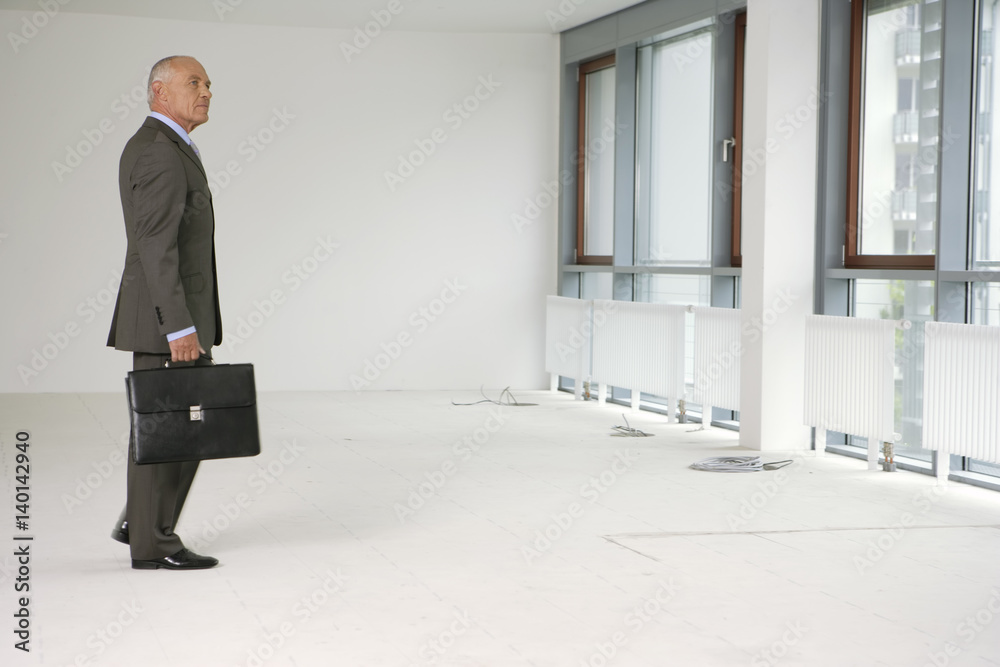 Fototapeta premium Elderly manager with briefcase, standing in an empty office