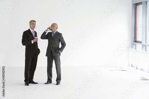 Two managers standing in an empty office, having a cup of coffee
