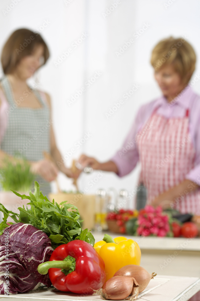 Two women preparing salad, several vegetables in foreground