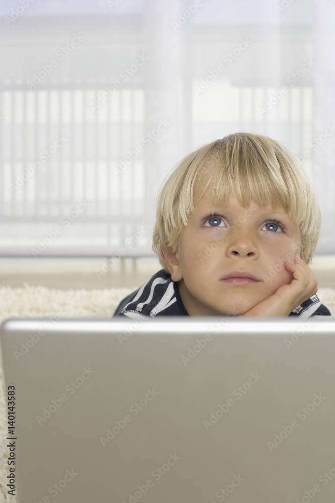 Boy (4-5 Years) lying in front of a laptop and looking up Boy (4-5 Years) lying in front of a laptop and looking up