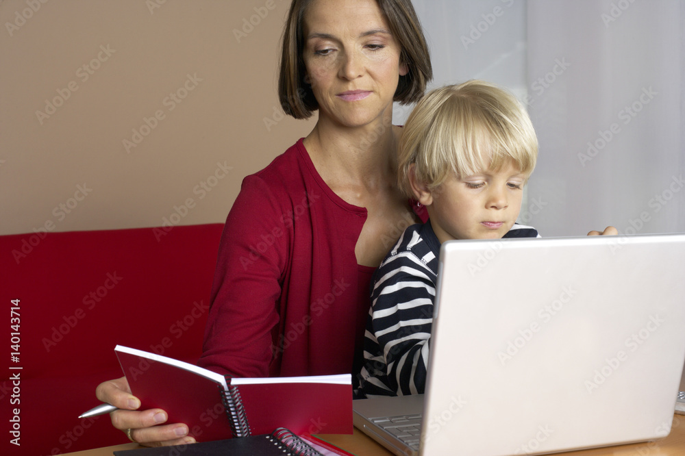 Mother reading a notebook while son (4-5 Years) sitting on her lap