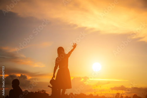 a silhouette of a happy young girl child the arms of his loving mother for a hug, in front of the sunset in the sky on a summer day.